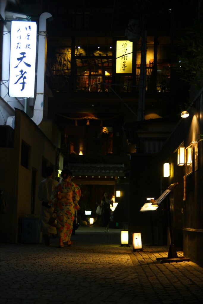 Geisha walking in a hanamachi alley at dusk