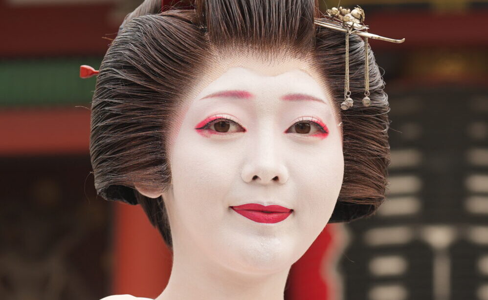 Close-up of geisha white oshiroi makeup and red lips with traditional kanzashi hair ornaments