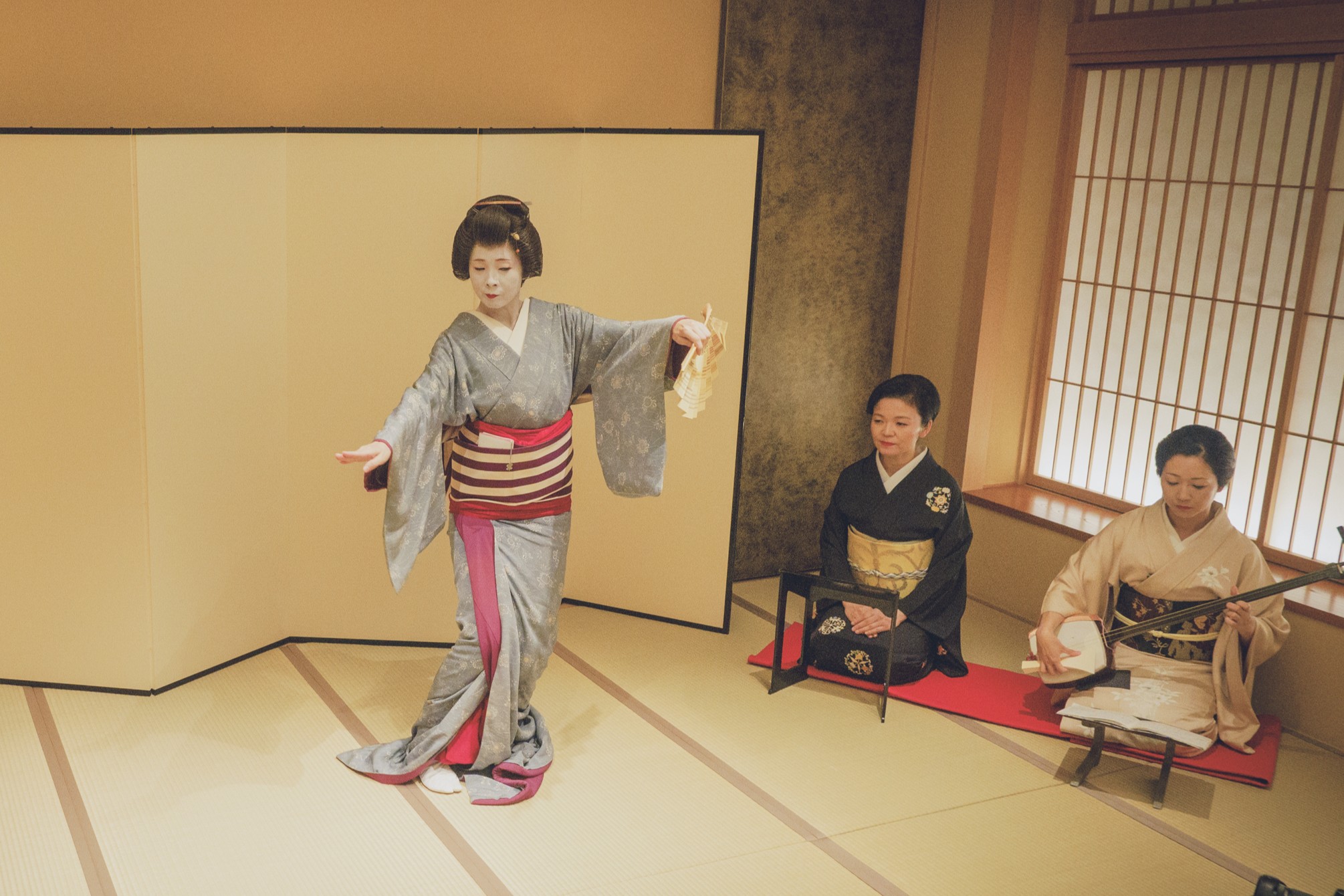 Jikata geisha playing shamisen beside tachikata geisha dancing in the tatami room
