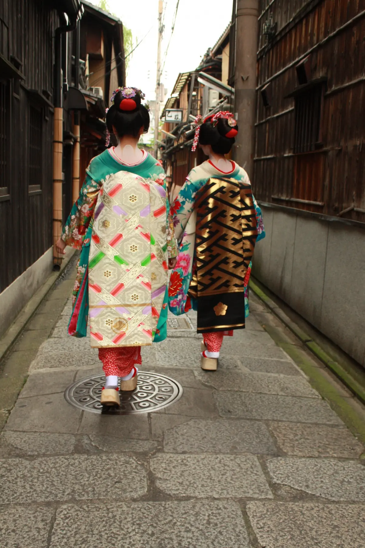 A maiko in full traditional dress showing long trailing sleeves, darari obi sash, and okobo wooden sandals