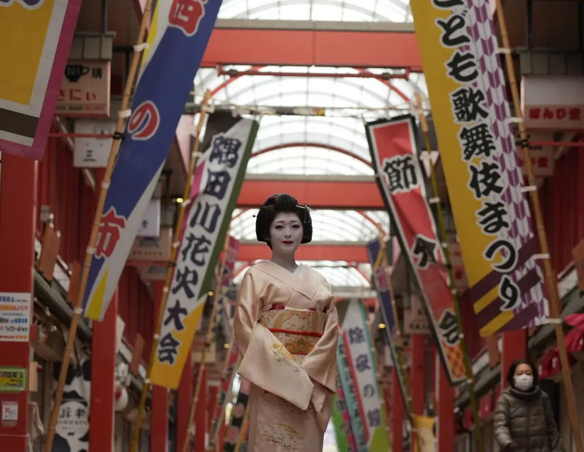 Geisha in a pale pink kimono walking through a colorful covered shopping arcade with vertical banners.