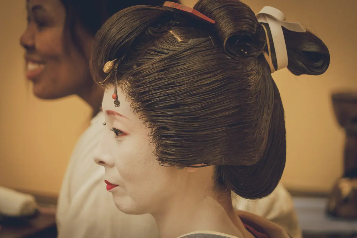 Geisha with white makeup and red lips in a traditional updo, profile view facing left