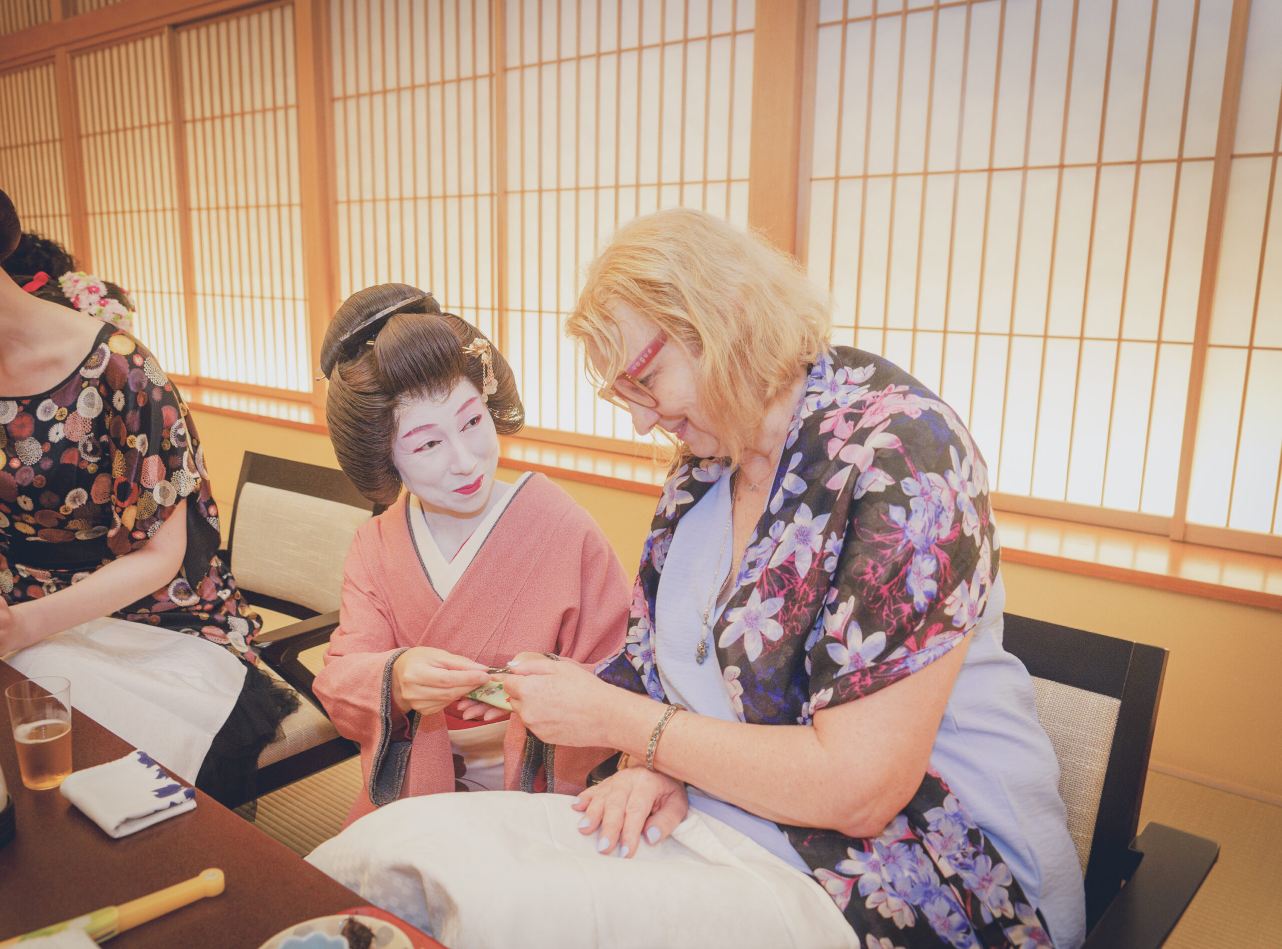 An Asakusa geisha in a pink kimono sharing a parlour game with two international guests in a private tatami room at Miyakodori