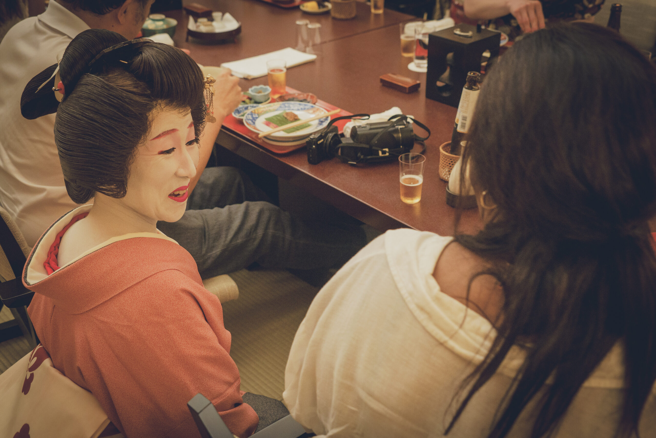 A geisha in a pink kimono sharing an intimate banquet with an international guest at a low table