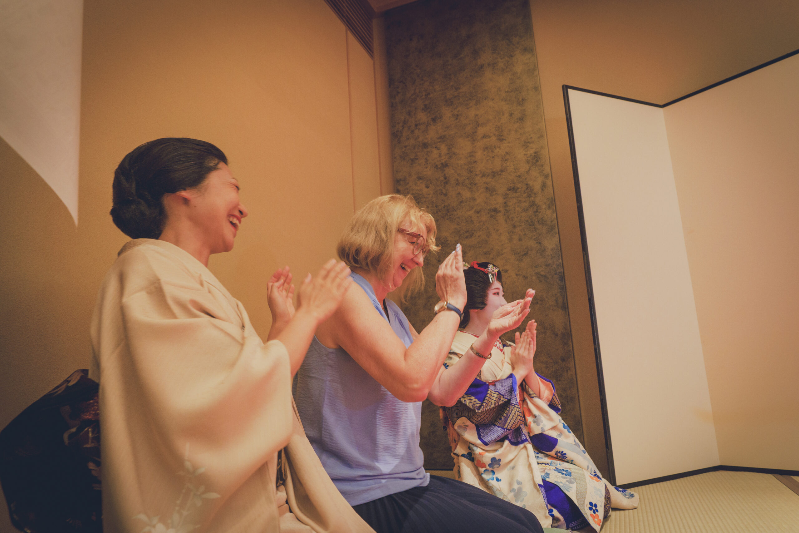 Asakusa geisha sharing a warm, smiling conversation with guests at an ozashiki — the gathering that was a teahouse's only real source of income