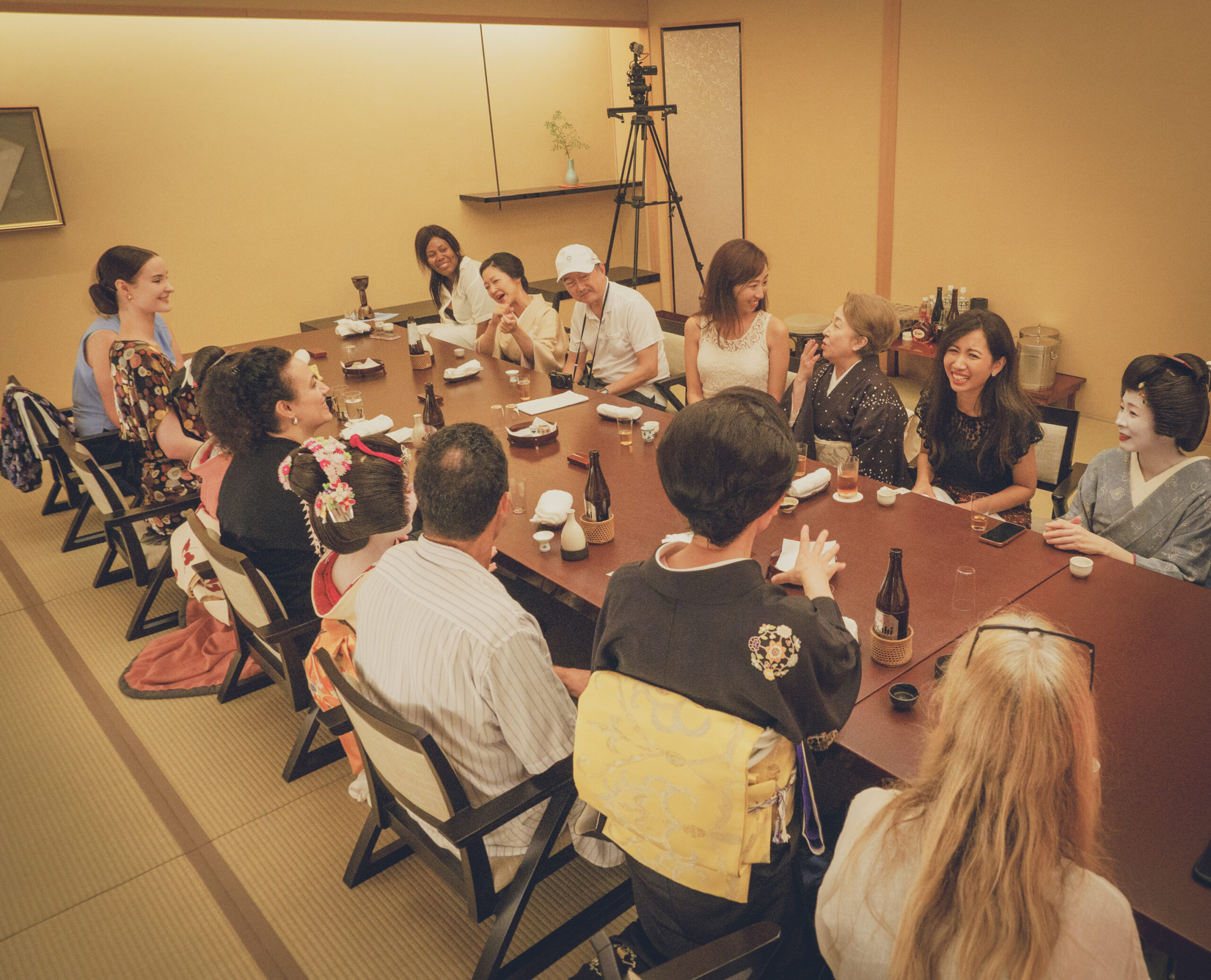 A lively ozashiki banquet at Miyakodori with geisha, a taikomochi entertainer, and international guests around a low table