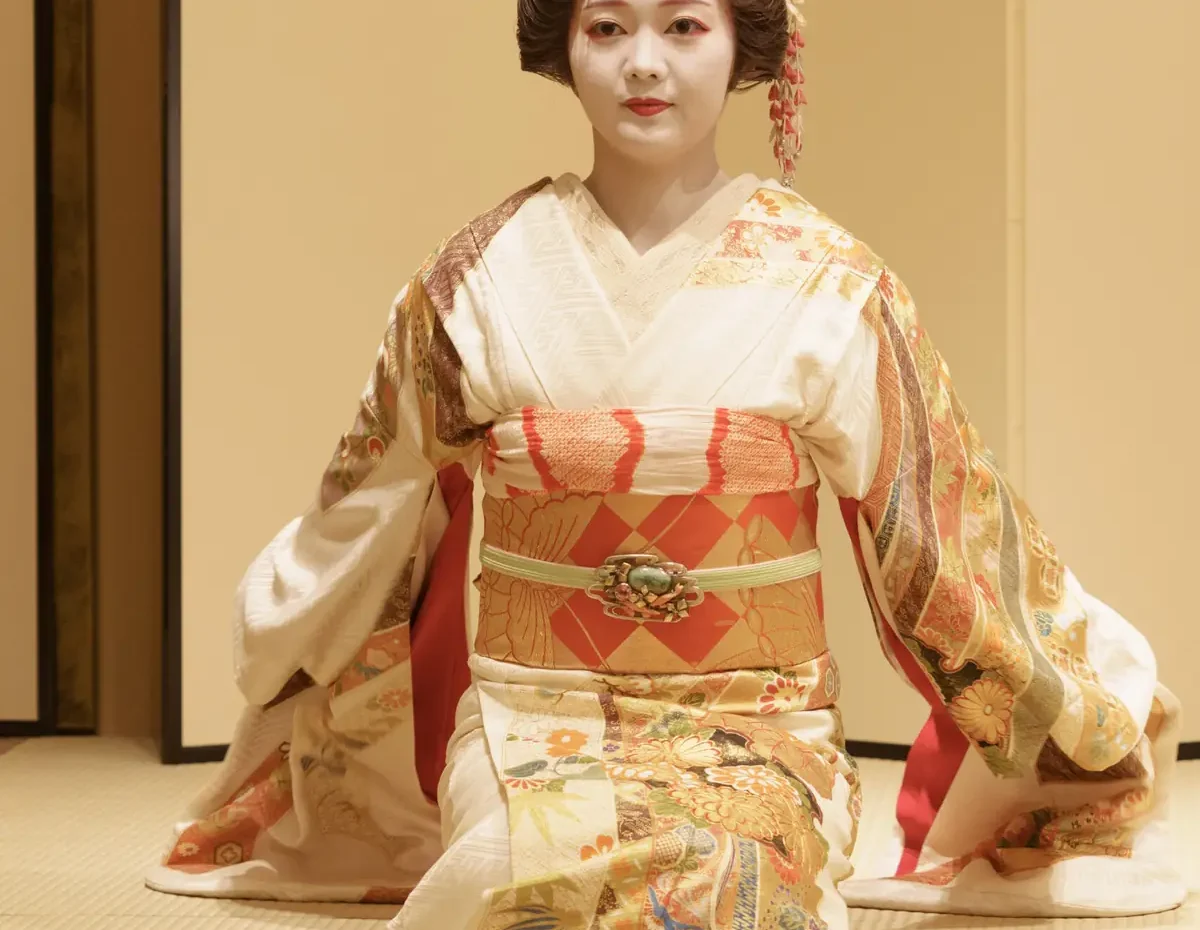Geisha in an ornate kimono kneeling on tatami, with a traditional updo and floral hair ornaments.