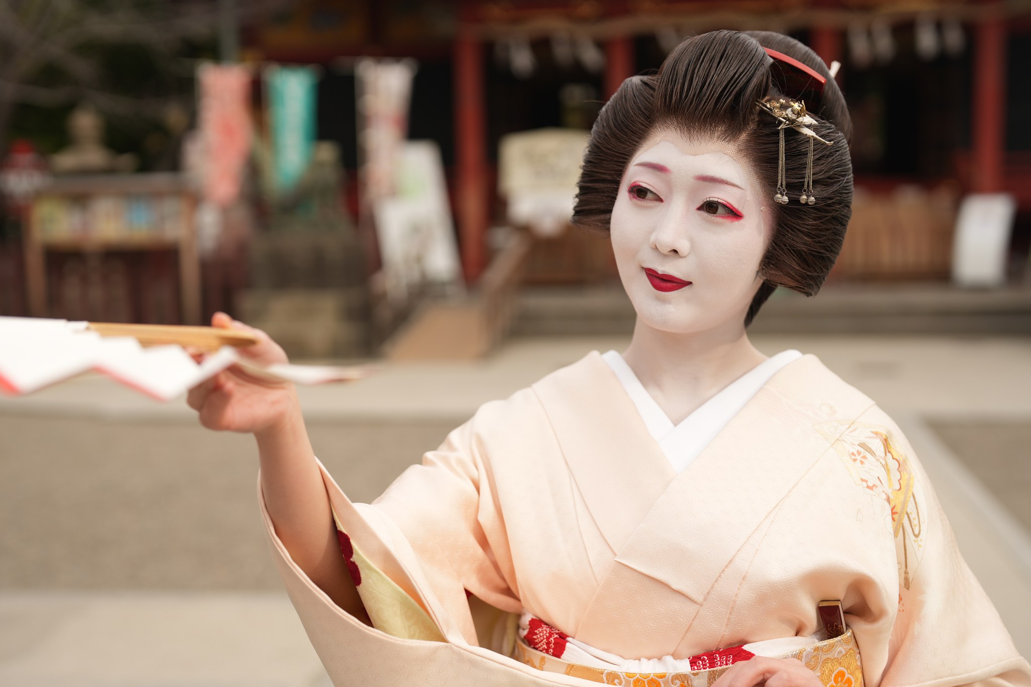 An Asakusa geisha in a pale pink kimono raising a folding fan mid-dance