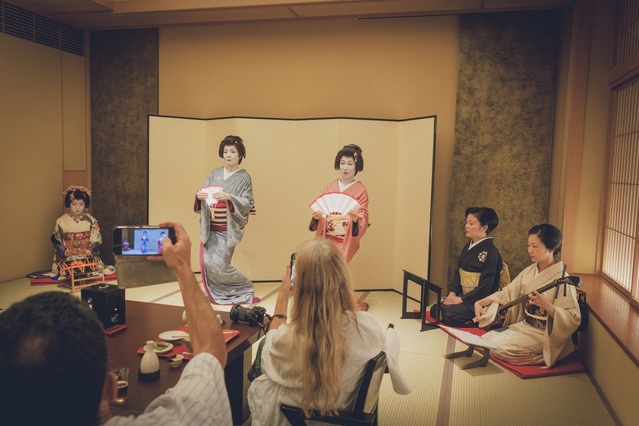 Overseas guests watching and photographing a geisha's dance up close at an ozashiki