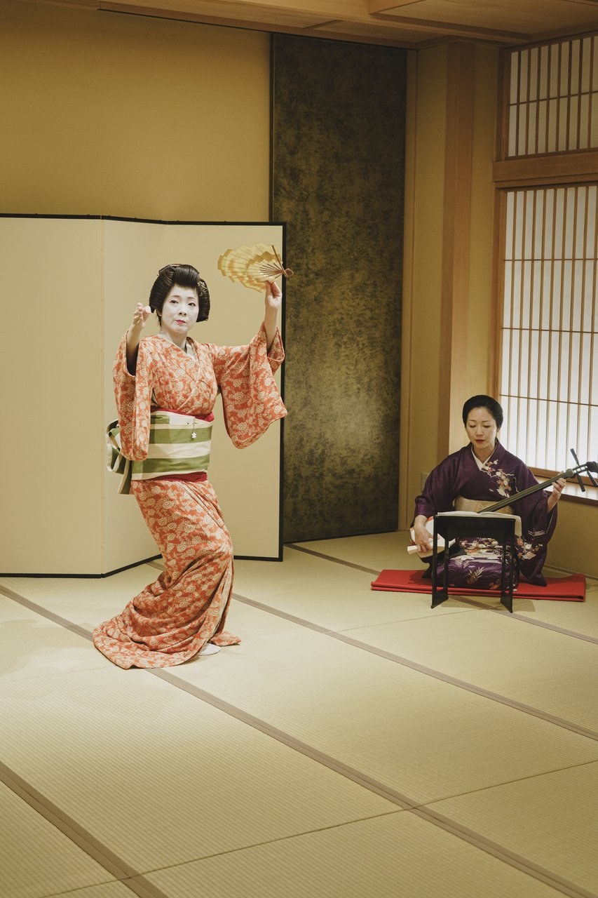 Two Asakusa geisha performing — one playing shamisen, one dancing — at a private ozashiki at Miyakodori