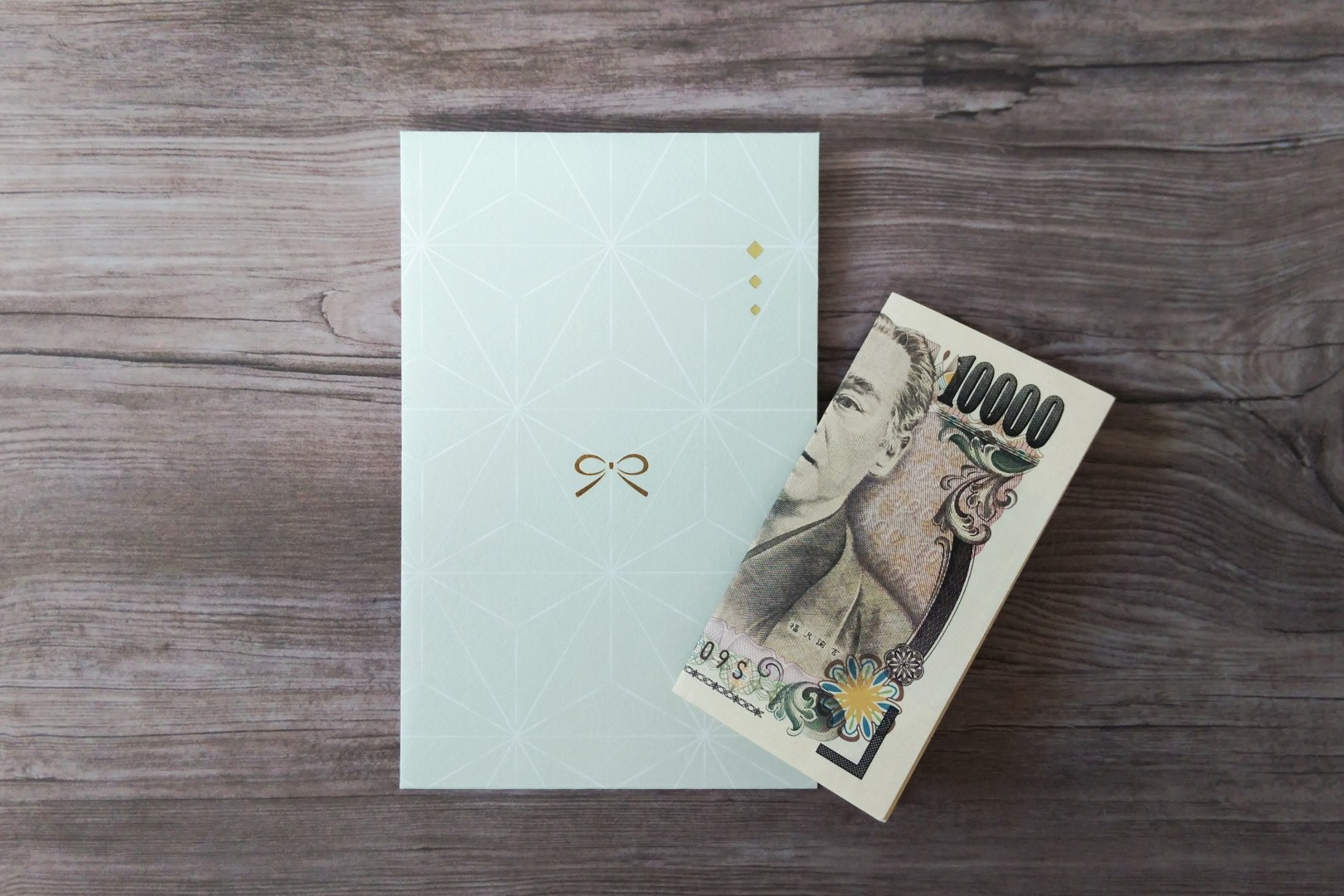 A decorative mint-green pochi-bukuro envelope used for goshugi at a geisha dinner, with crisp ¥10,000 notes, on a wooden table at Miyakodori in Asakusa