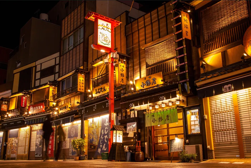 Nighttime street in Japan with illuminated lanterns and traditional storefronts along a narrow lane.