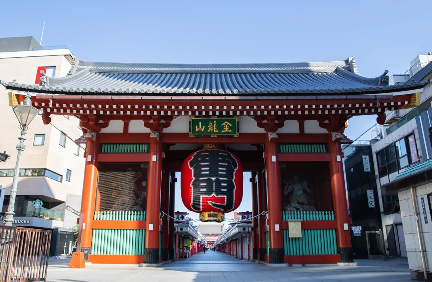Kaminarimon gate at Senso-ji temple with a large red lantern hanging between red pillars and a long shopping street beyond.
