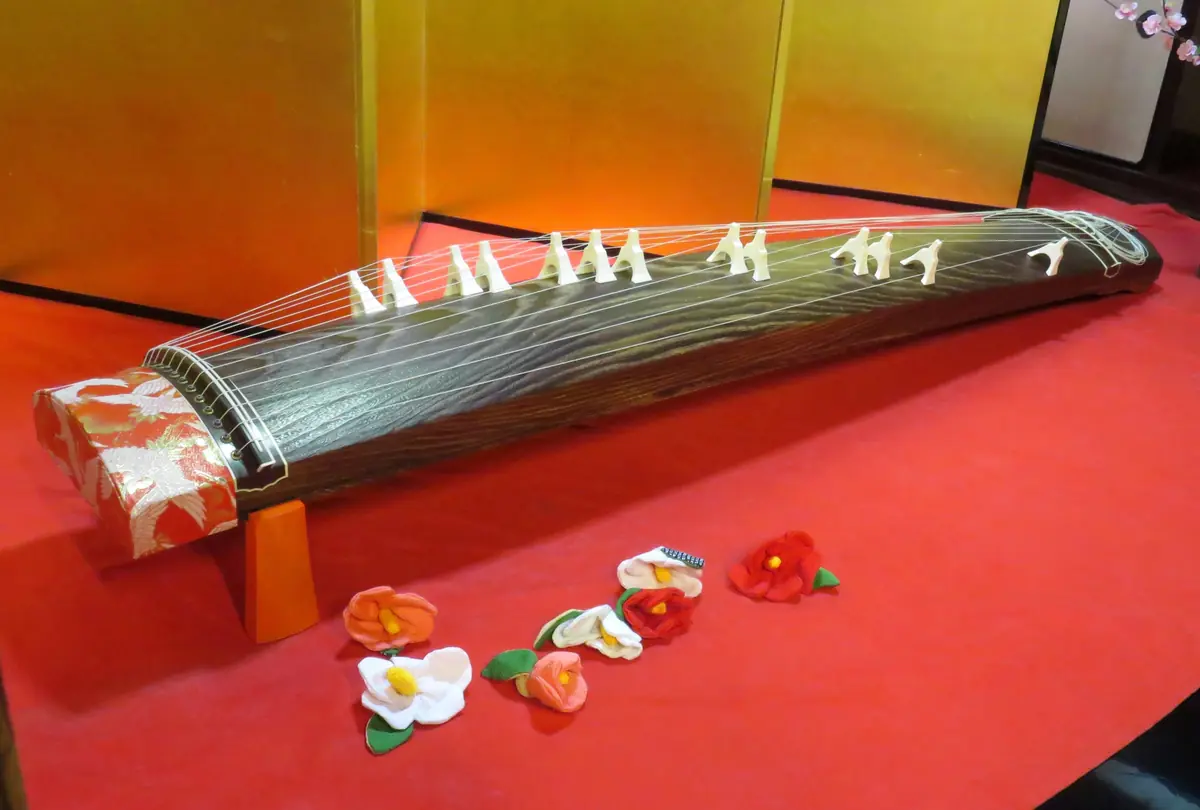 A traditional Japanese koto resting on a red table with white turnable bridges and decorative flowers laid in front for display.