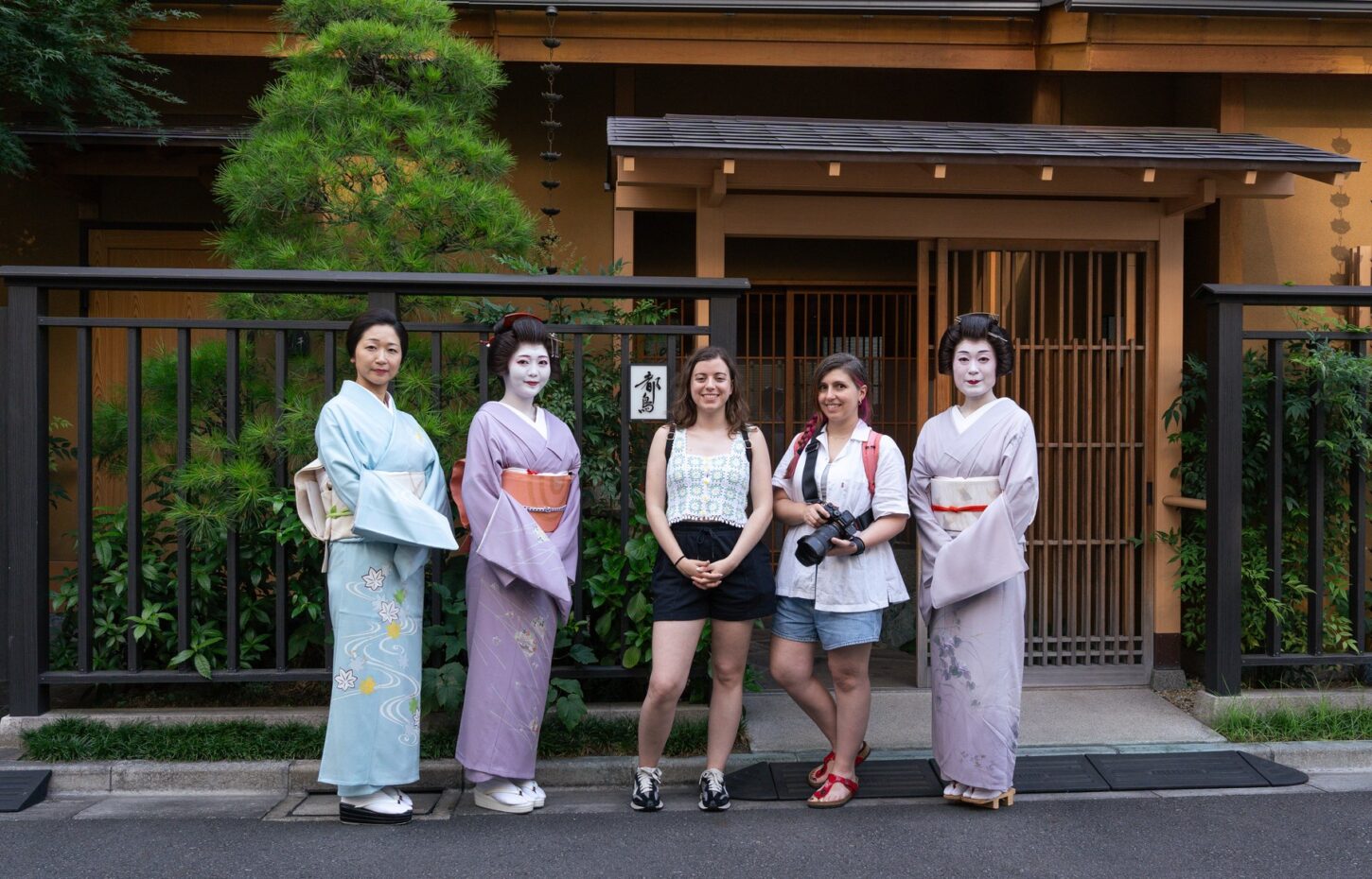 Three Asakusa geisha in pastel kimono posing with two international guests at a machiai-chaya