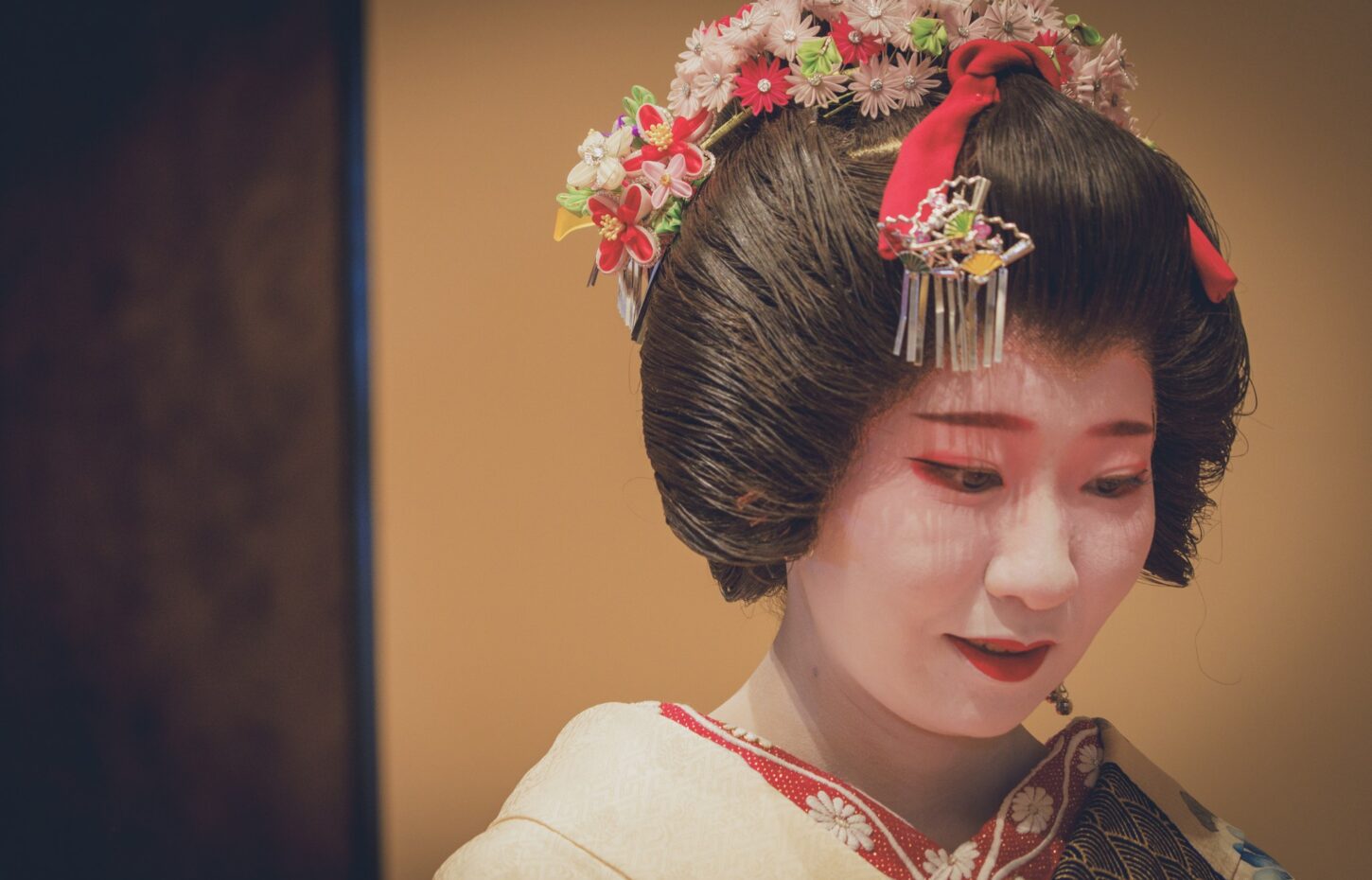 An Asakusa geisha in a cream kimono with a floral hair ornament in warm light
