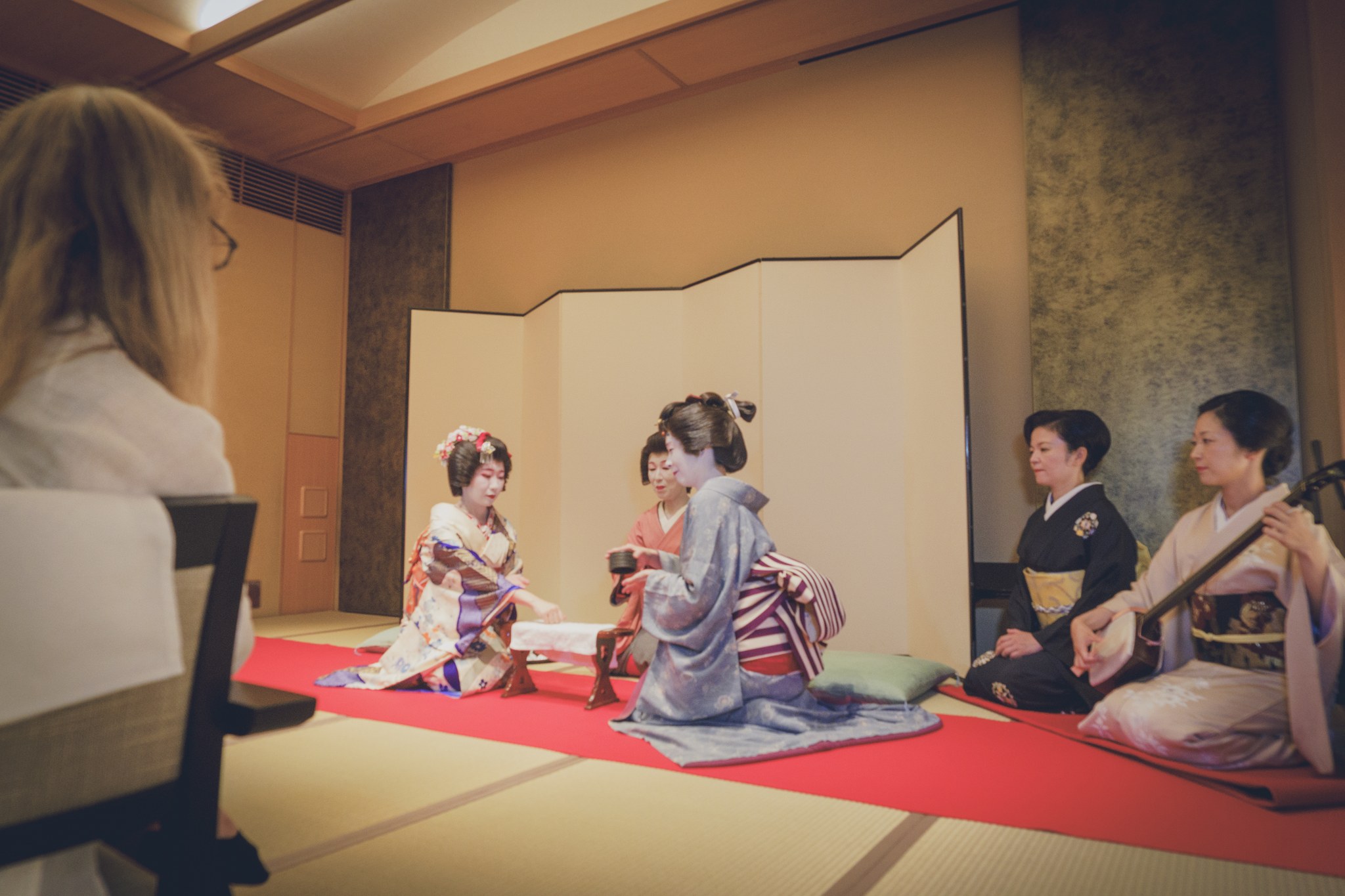 A geisha preparing matcha tea beside a shamisen player at a traditional ozashiki