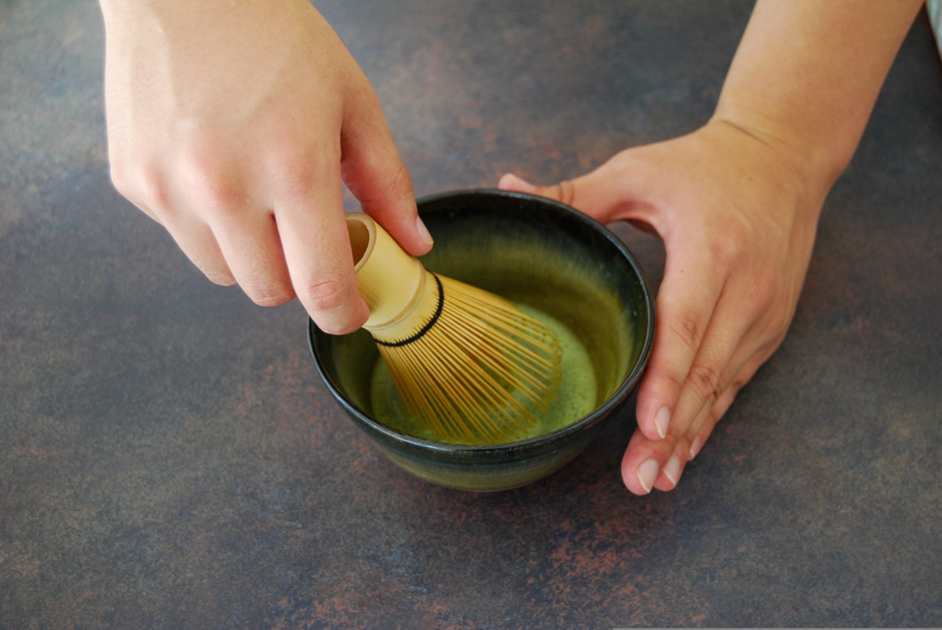 Close-up of hands whisking matcha with a bamboo whisk in a tea bowl