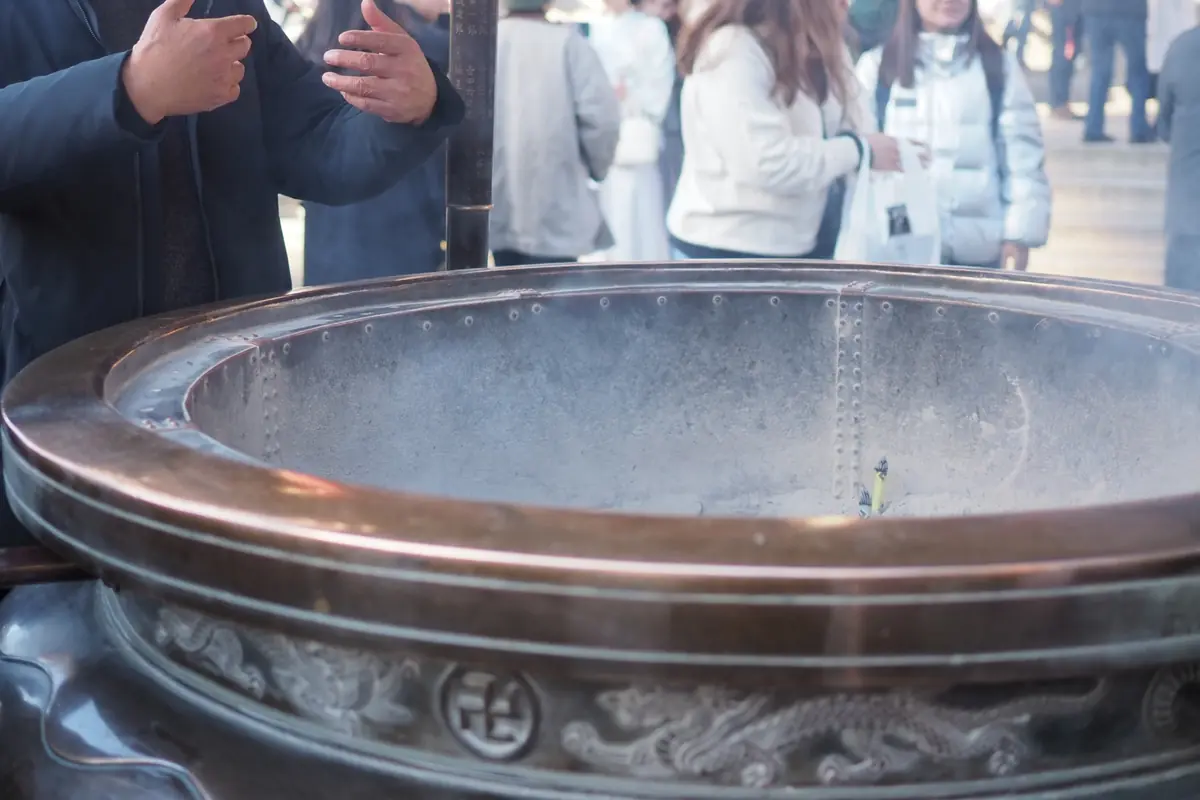 Visitors wafting incense smoke at the large incense burner in front of Senso-ji Temple main hall