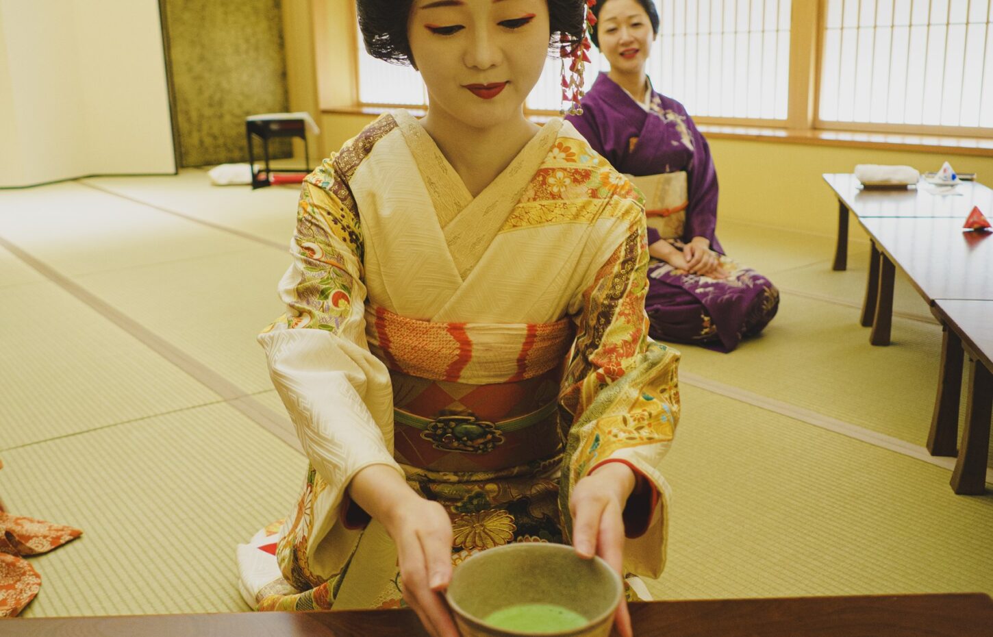 An Asakusa geisha offering a bowl of matcha with both hands at Miyakodori — matcha with geisha in Tokyo's Asakusa flower district