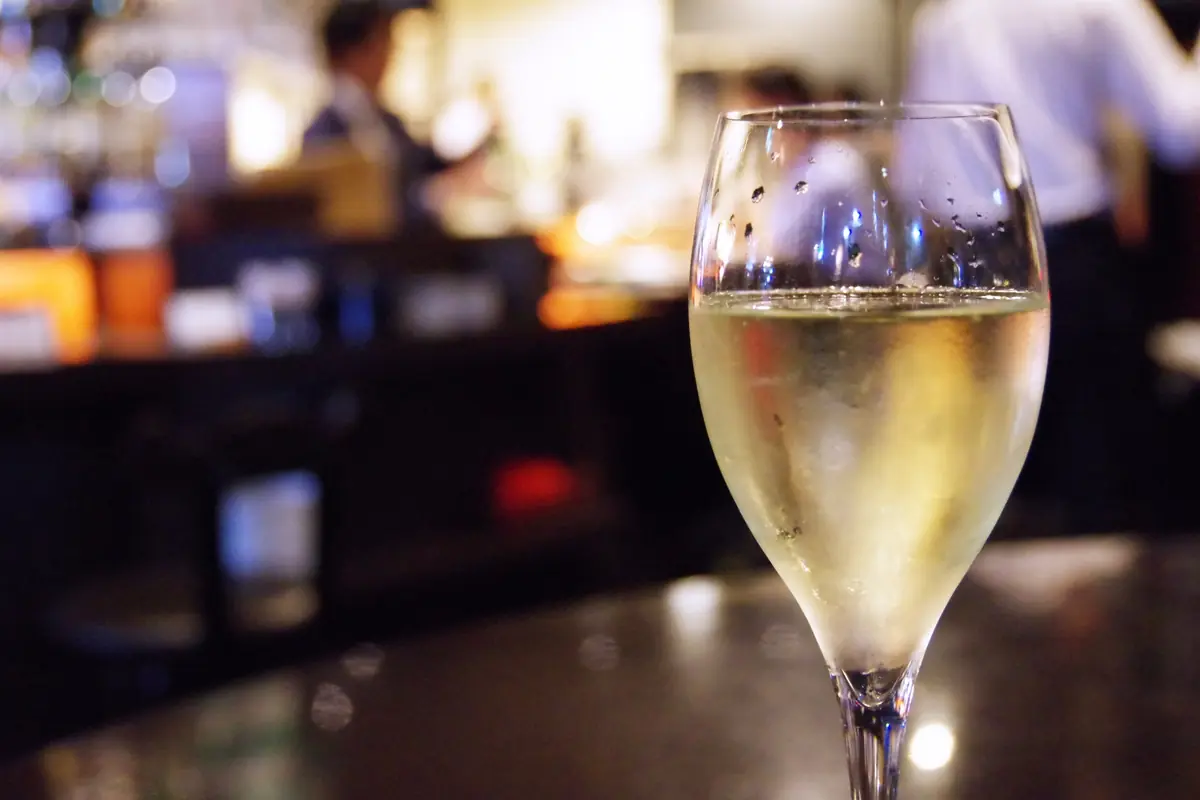 A stemmed glass of white wine on a dark bar counter with a blurred bar/restaurant background.