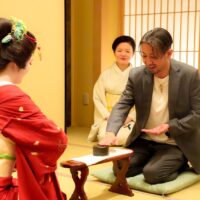 An ozashiki game of konpira fune fune being played at Miyakodori — guests and geisha face each other at a low lacquered armrest, tapping in rhythm