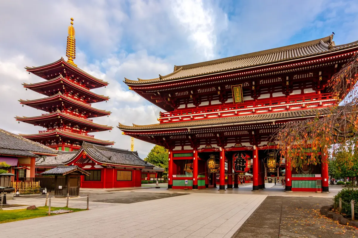 Red-lacquer Japanese temple gate with a five-story pagoda in the background and a wide stone courtyard.