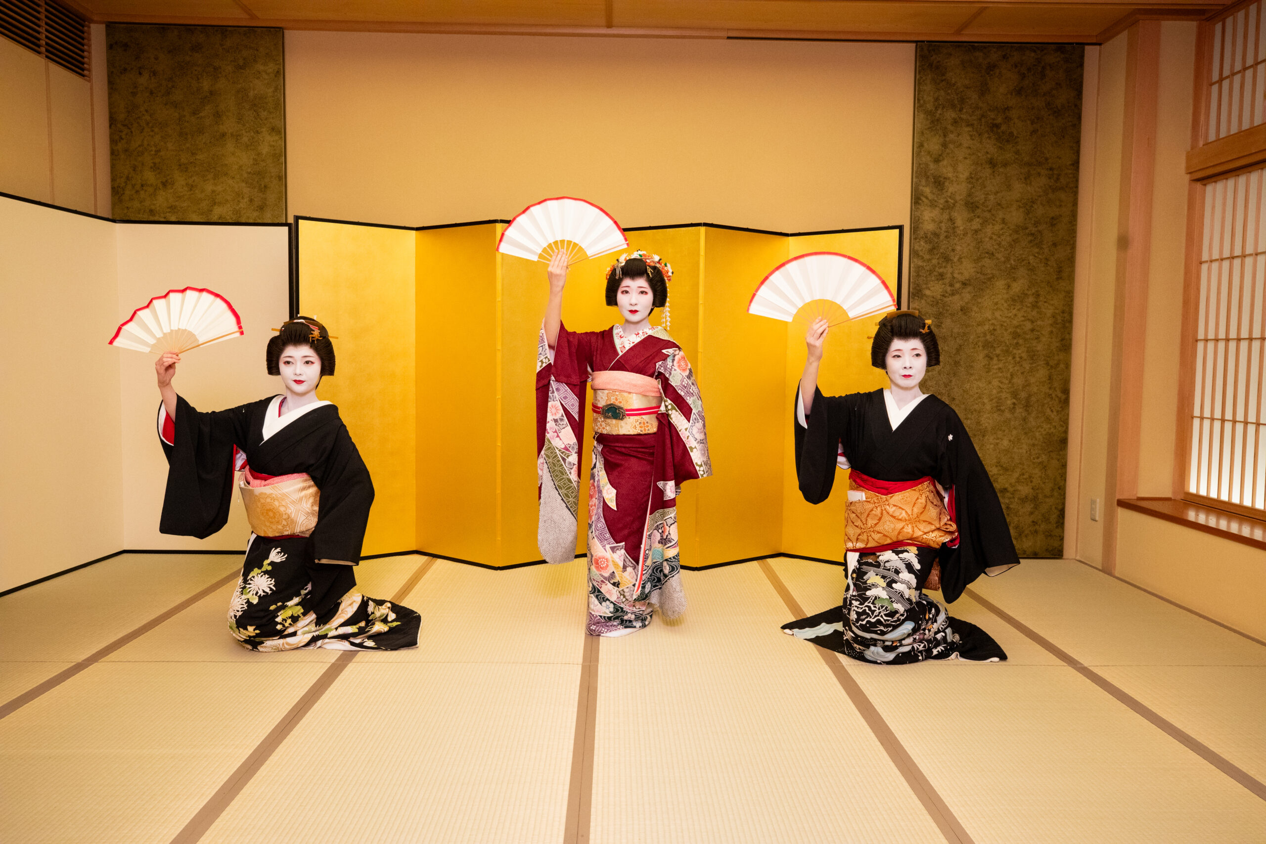 Three geisha performing a fan dance before a golden folding screen