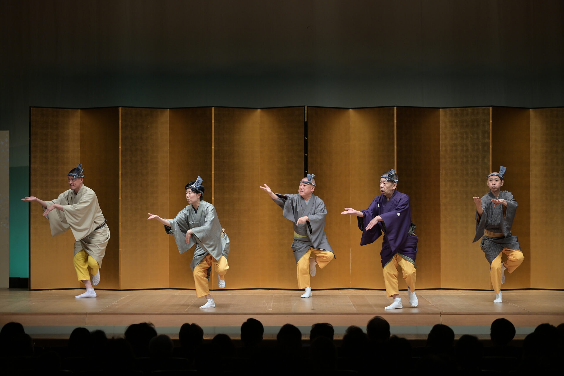 Hōkan entertainers performing together on stage before a golden folding screen