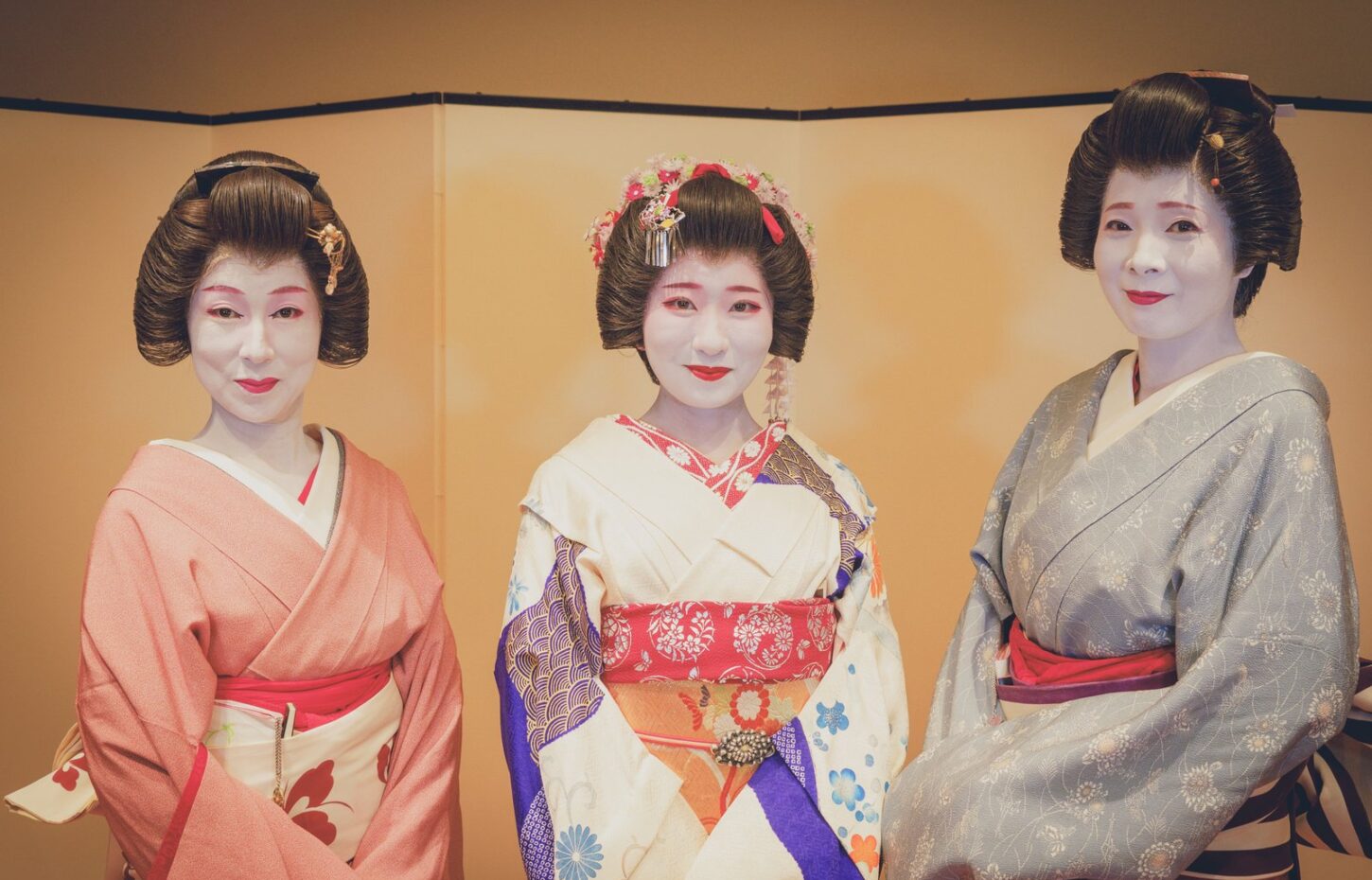 Asakusa geisha at Miyakodori - Authentic Geisha Experiences | Miyakodori Three Asakusa geisha in formal kimono before a plain folding screen at Miyakodori