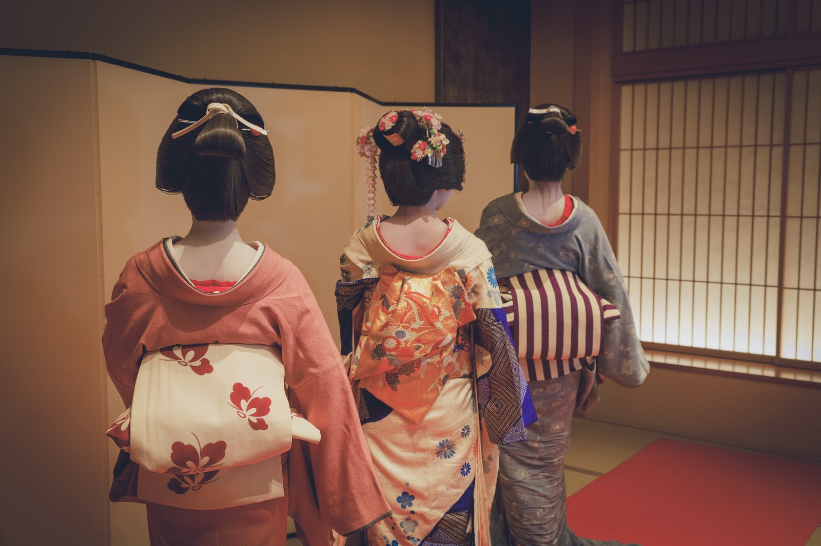 Three Asakusa geisha seen from behind, showing three different nihongami hairstyles and obi knots