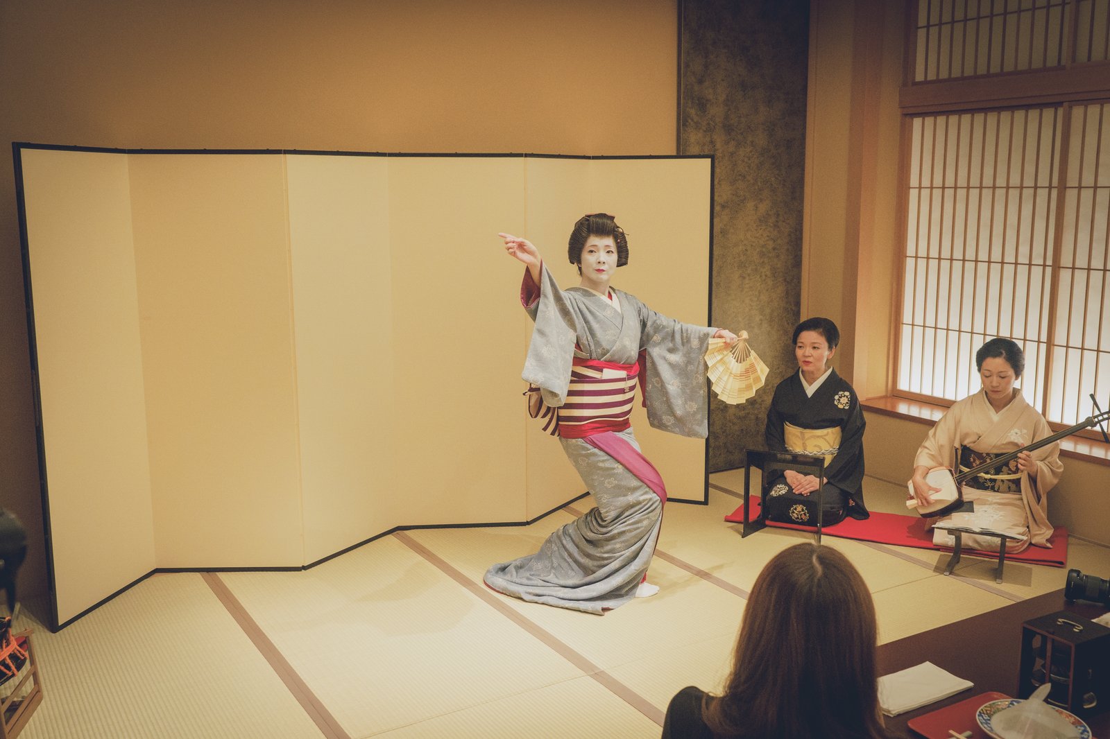 A jikata playing shamisen beside a tachikata dancing at a Miyakodori ozashiki