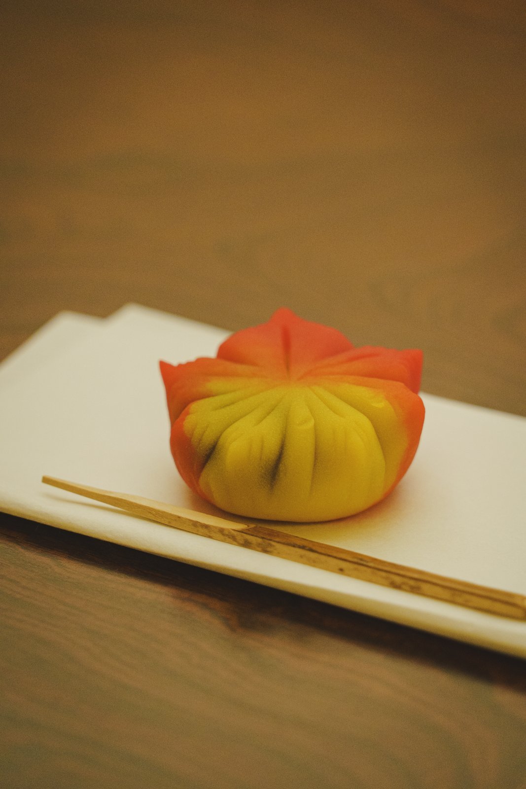 A maple-shaped autumn wagashi on white paper with a bamboo pick, the sweet course of a seasonal kaiseki at Miyakodori