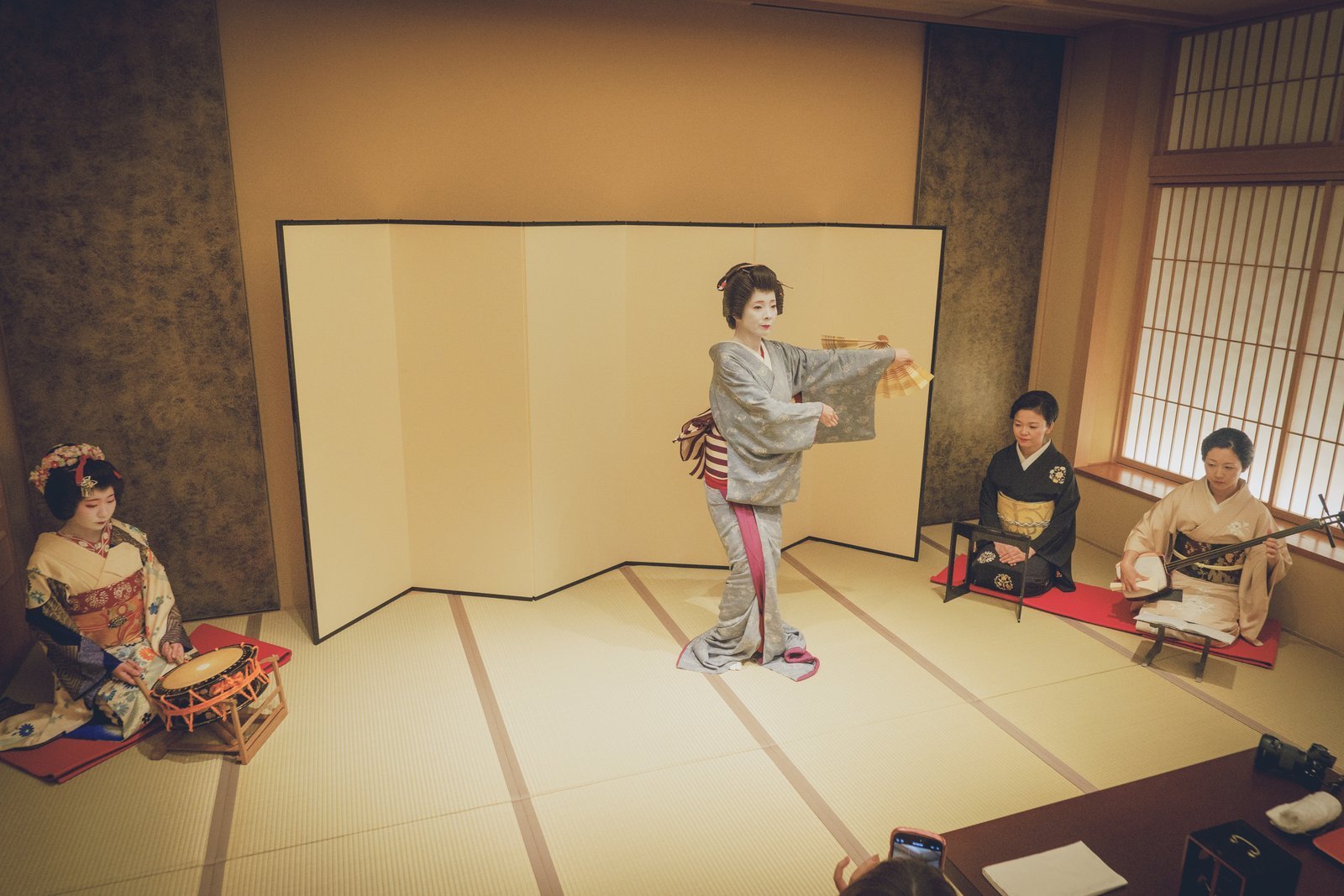 An Asakusa geisha dancing with a fan while three others play shamisen and hayashi percussion at Miyakodori