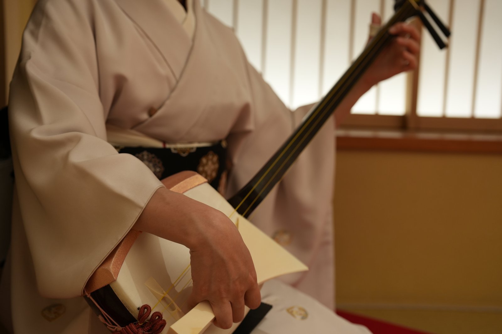 An Asakusa geisha playing the shamisen beside a shoji screen in the tatami room at Miyakodori