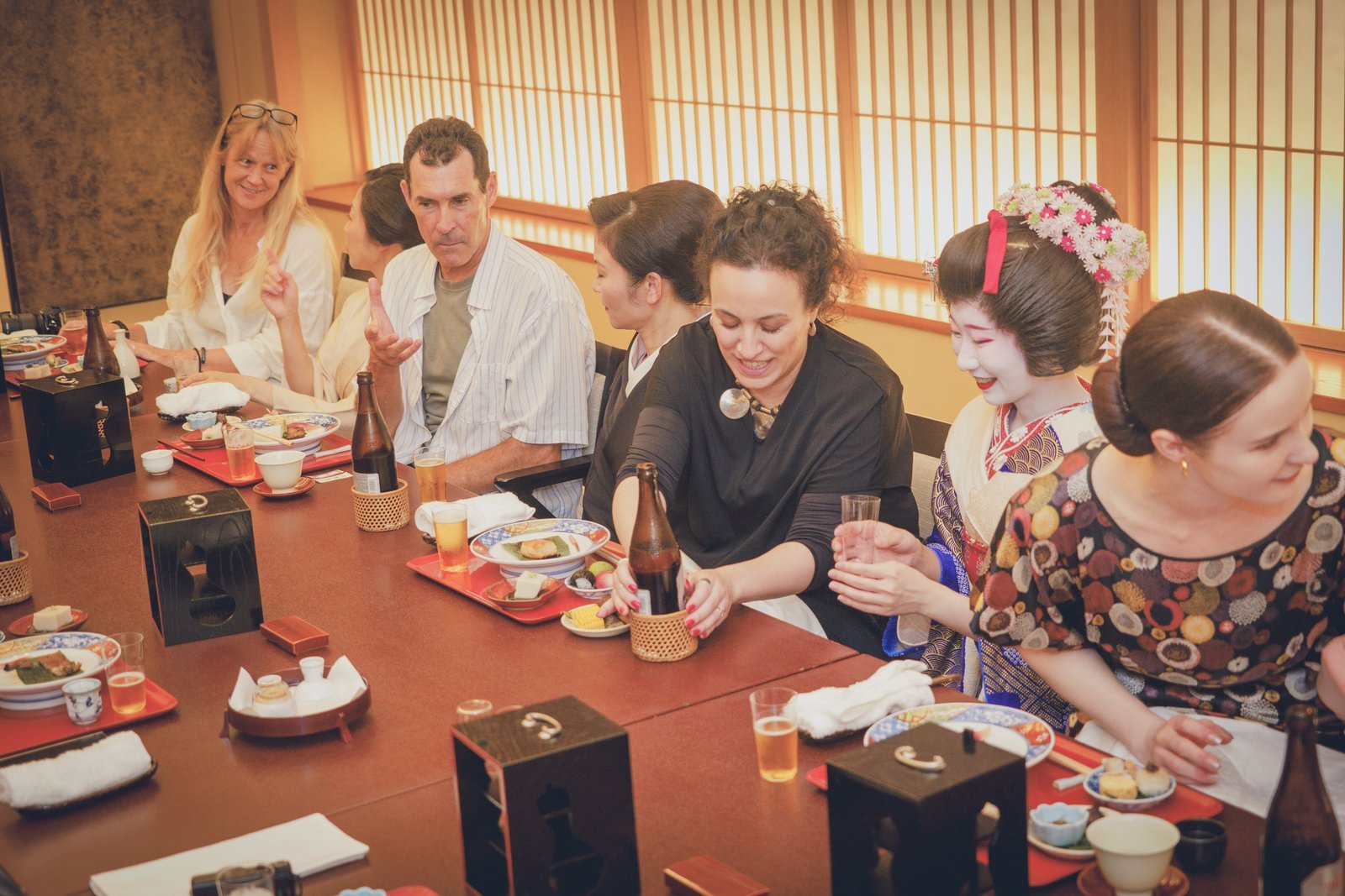Geisha pouring a drink for a guest and sharing conversation across the low table during an ozashiki at Miyakodori