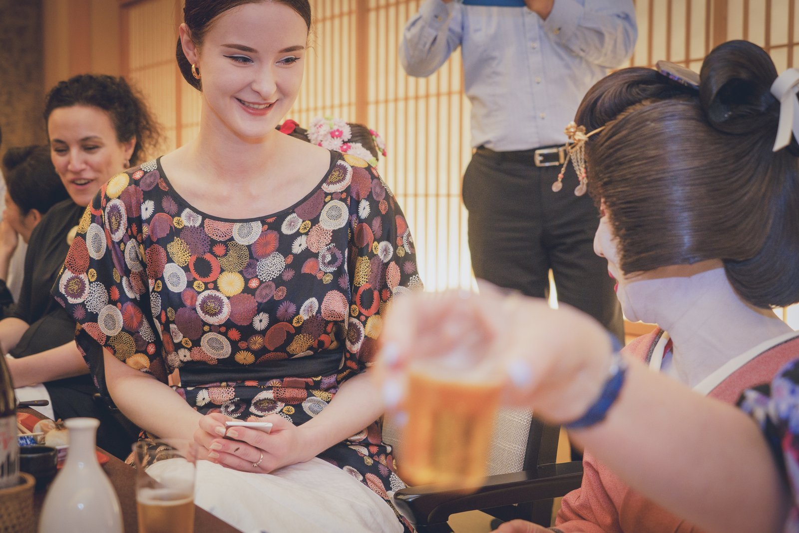 A geisha pouring sake for a guest at the low table of a tatami ozashiki room