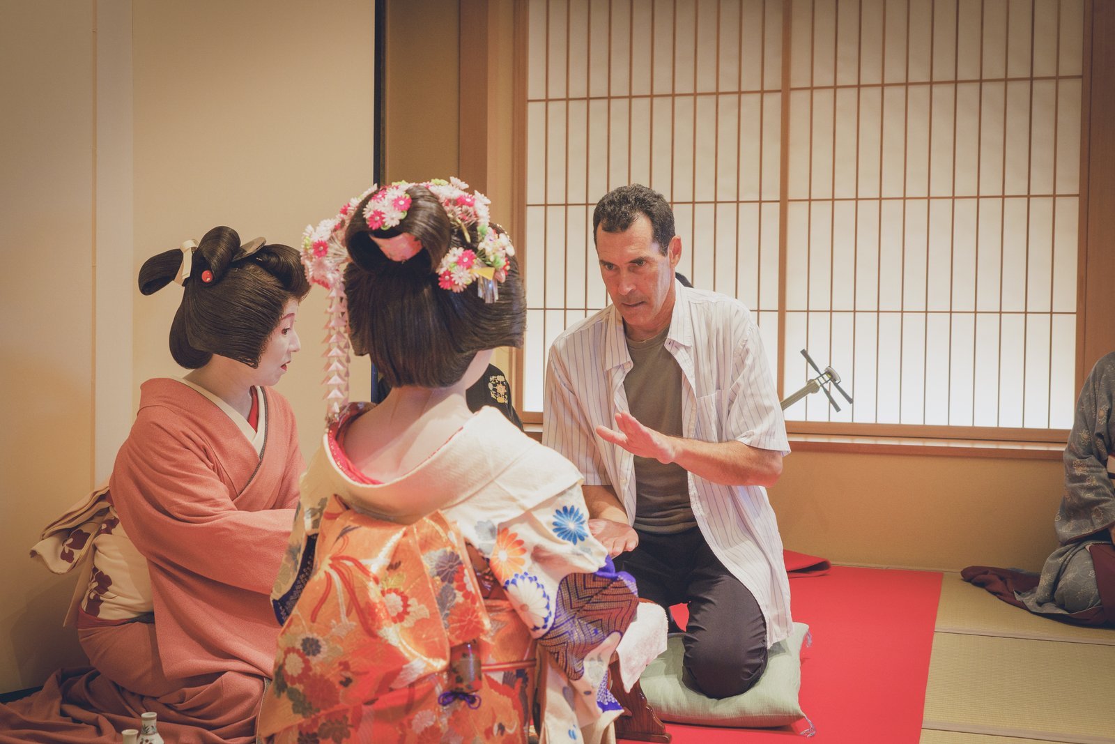 Guests and a geisha playing konpira fune fune, a traditional ozashiki asobi parlor game, around a small table
