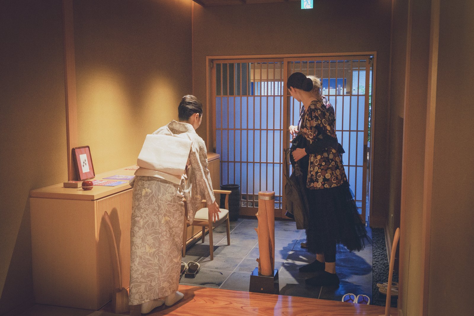 A guest stepping out of her shoes at the entrance of Miyakodori before going up to the tatami room, with footwear lined up on the stone floor