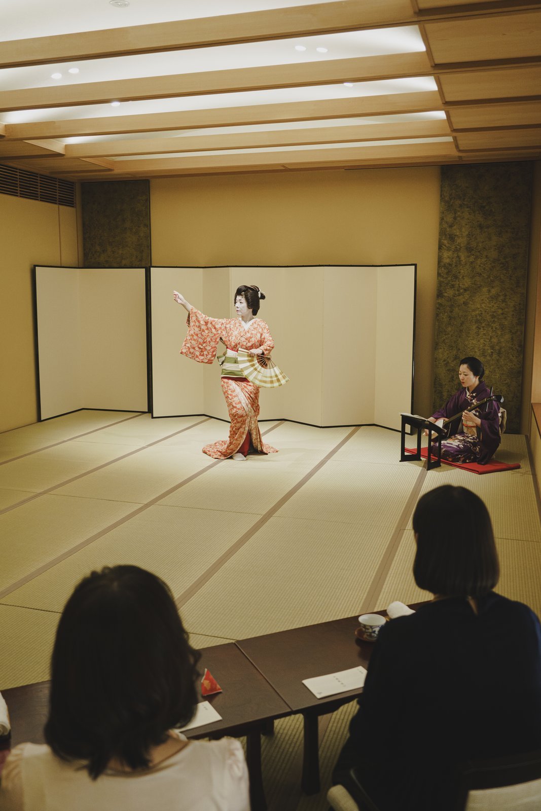 Guests watching an Asakusa geisha dance at an ozashiki, with a shamisen player seated nearby