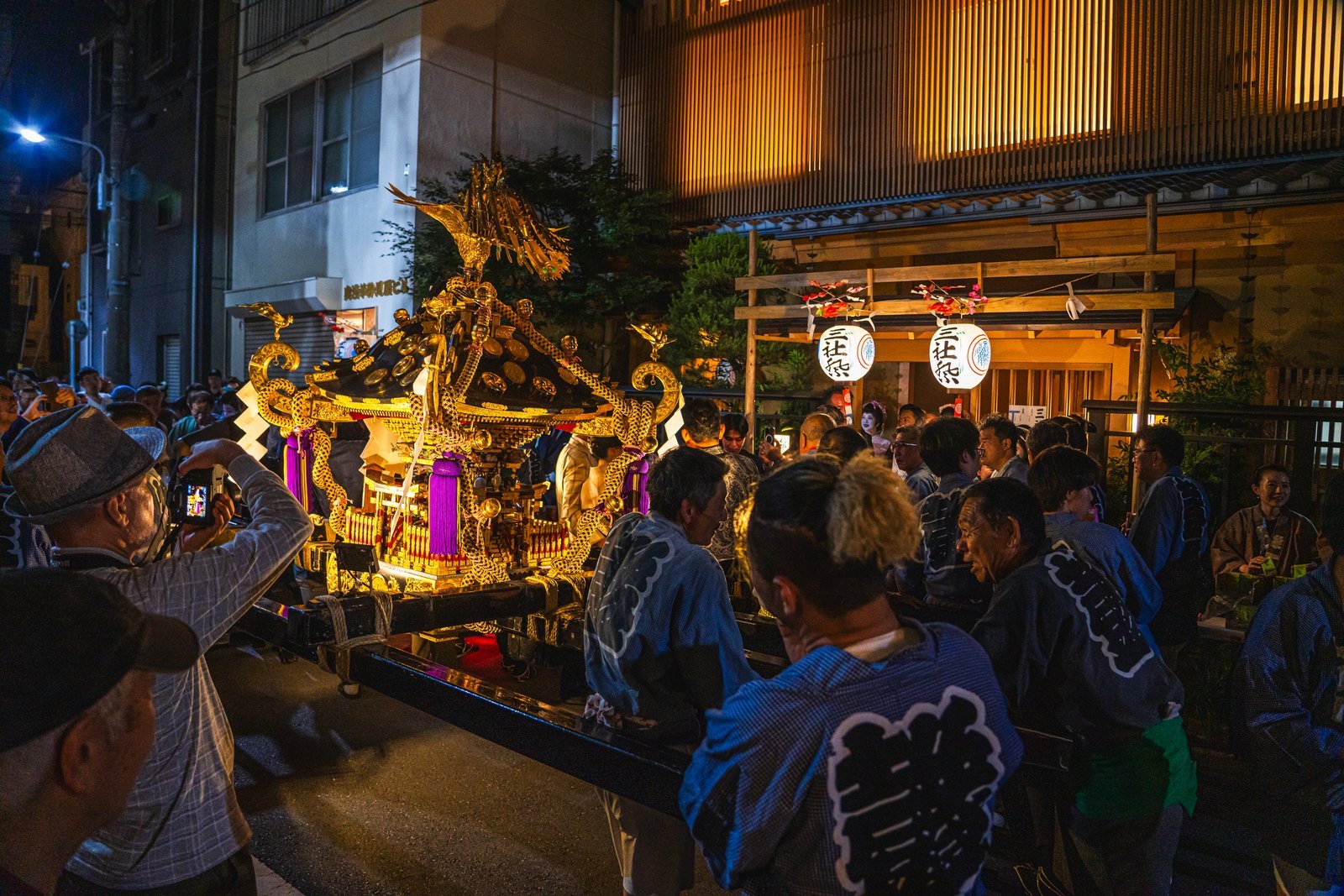 A mikoshi portable shrine surging down a narrow lane behind Senso-ji during Sanja Matsuri, surrounded by bearers in happi coats