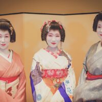 Three Asakusa geisha in formal kimono before a folding screen at Miyakodori, a machiai-chaya in Asakusa, Tokyo