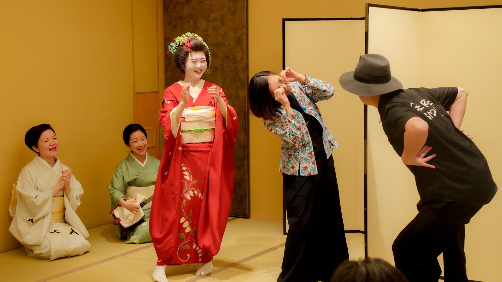 Two guests revealing their poses from either side of the byobu screen as the hangyoku and musicians look on