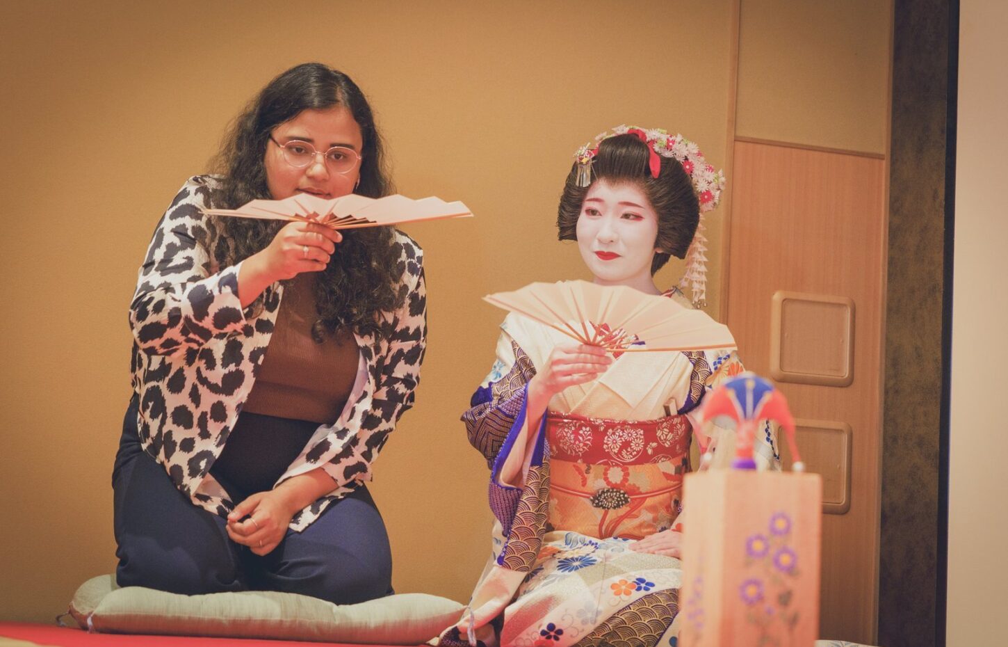 A guest and a geisha side by side, each raising a tosenkyo fan and ready to throw, at a Miyakodori ozashiki in Asakusa
