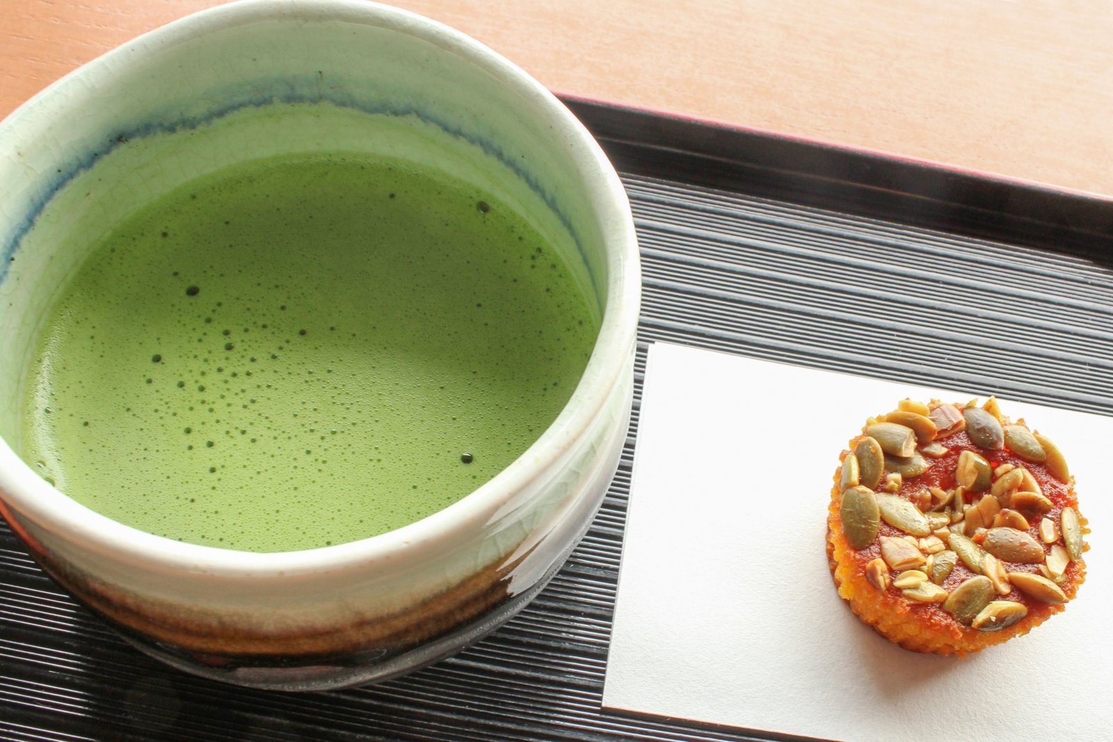 A bowl of whisked matcha served beside a small wagashi on a lacquer tray, the classic pairing of bitter and sweet