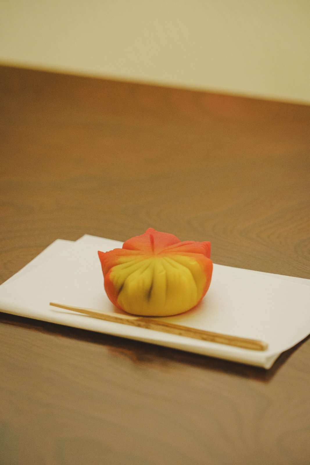 A single seasonal wagashi on a small plate, set down in front of a guest in a tatami room during a geisha evening