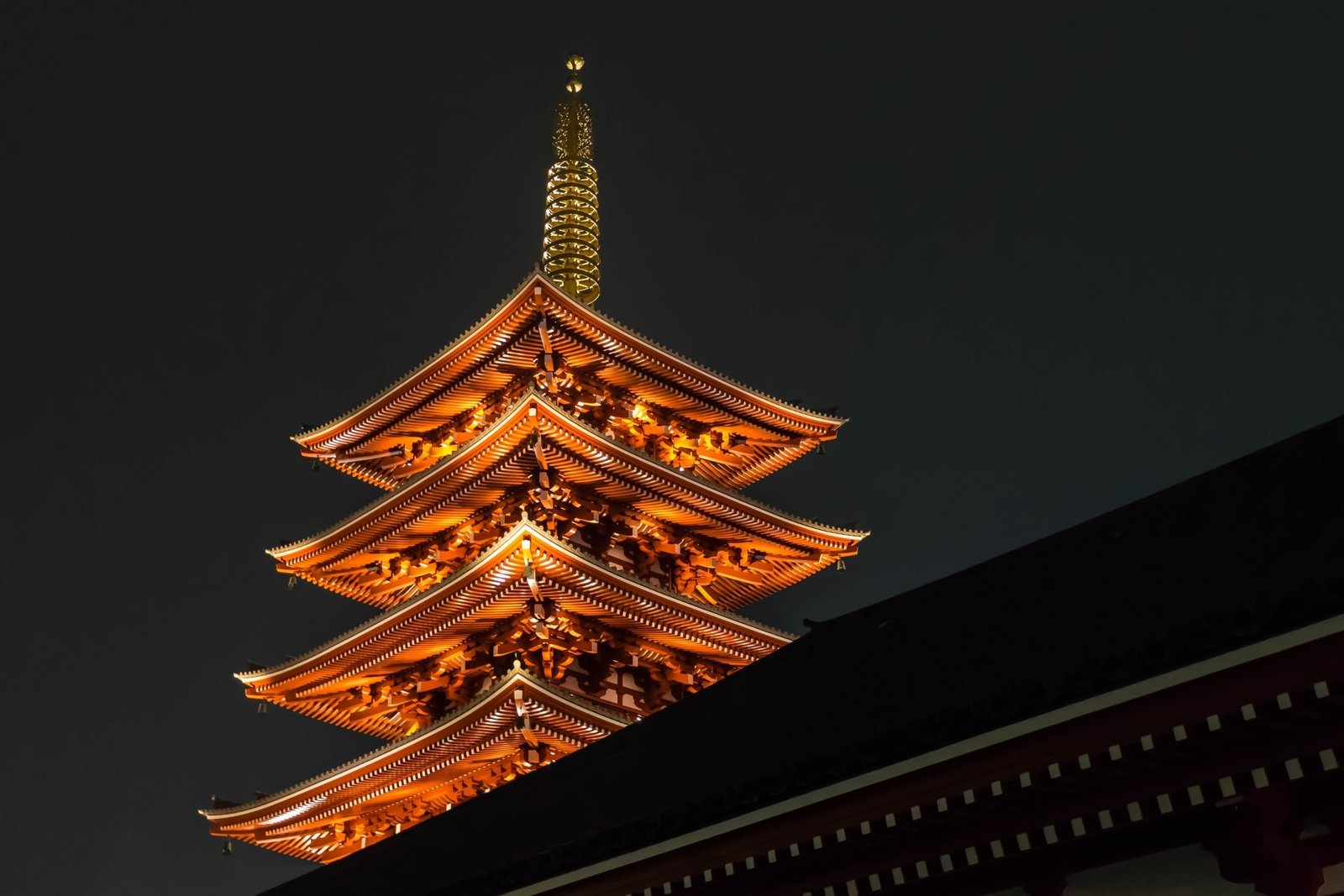 Senso-ji's five-story pagoda illuminated at night, vermilion and gold against a dark sky