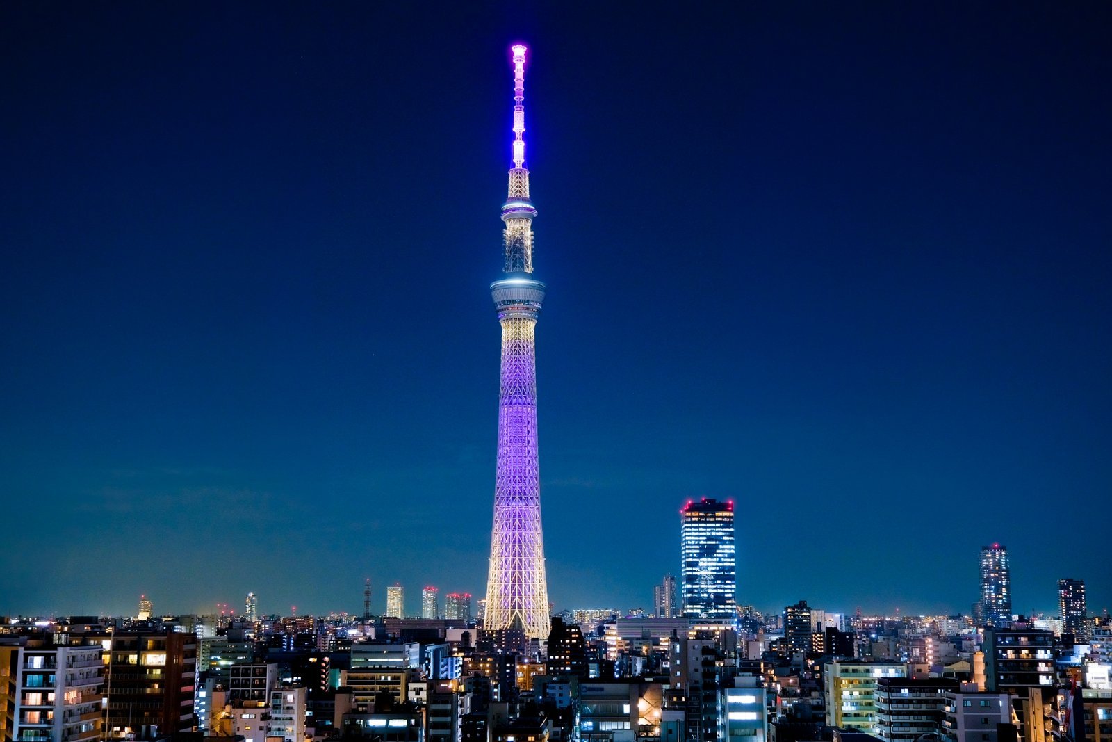 Tokyo Skytree illuminated in purple at night, with the city skyline in the foreground