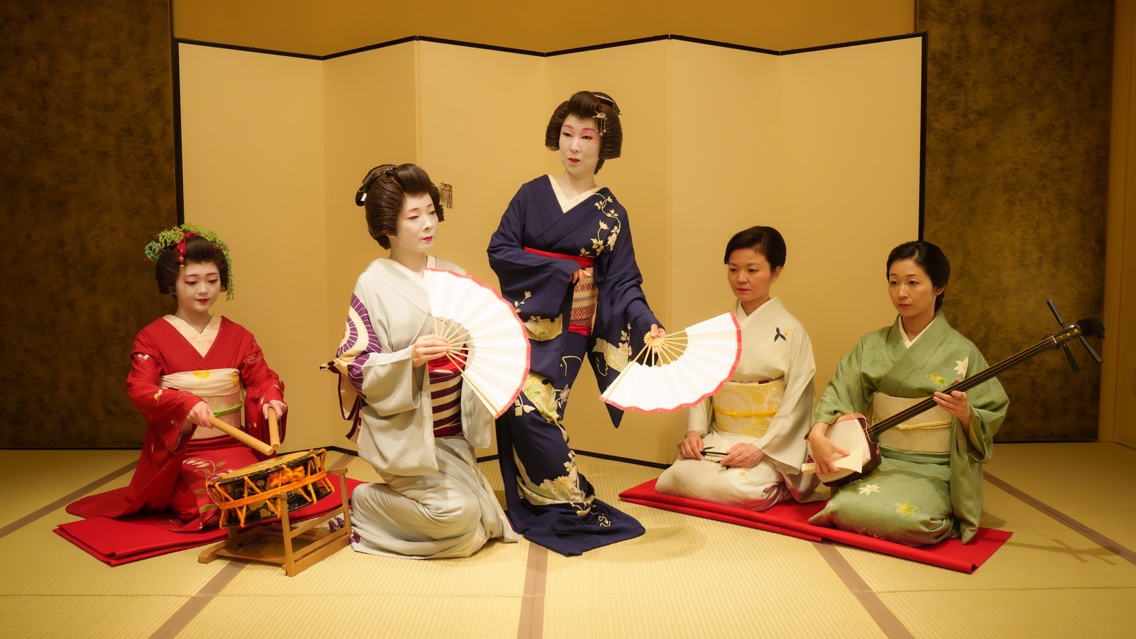 Asakusa geisha holding their fans out in a formal pose, with a hangyoku on the drum and jikata on shamisen