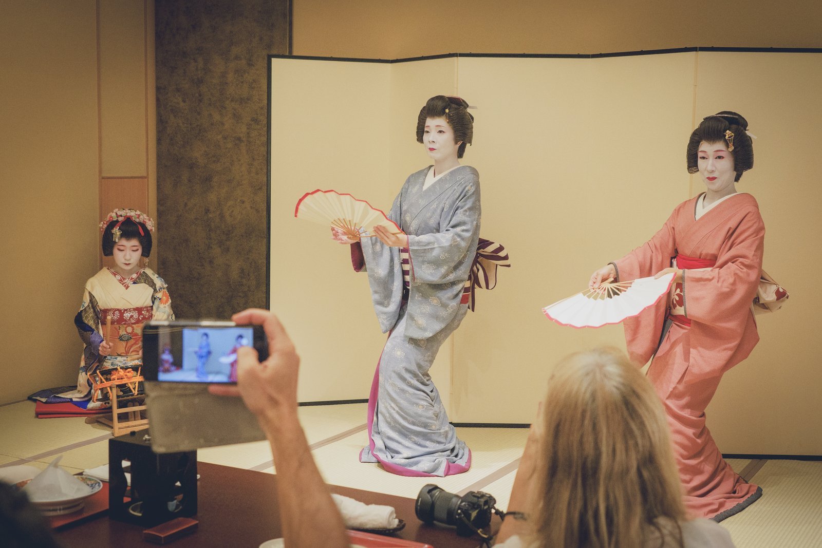Two Asakusa geisha dancing for guests at a private ozashiki while a guest films on her phone
